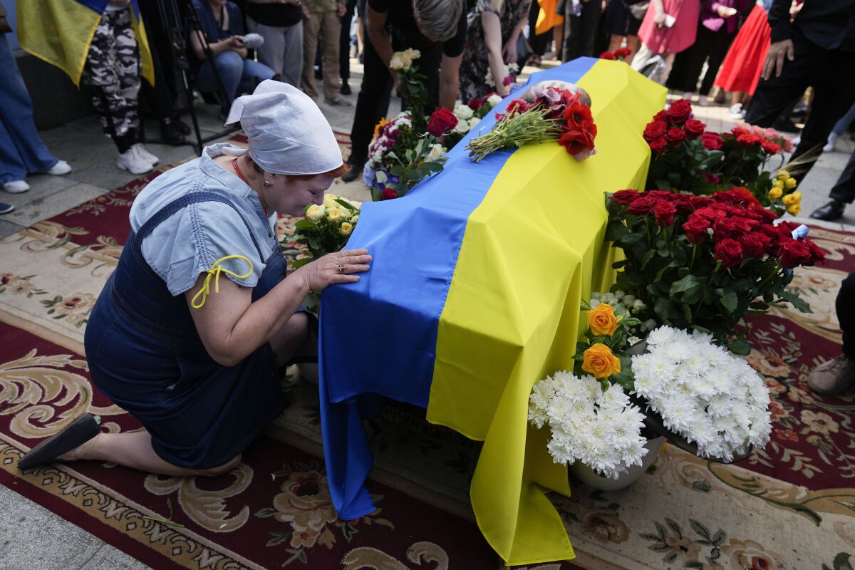  A woman kneels at activist and soldier Roman Ratushnyi's coffin during his memorial service in Kyiv, Ukraine on Saturday.