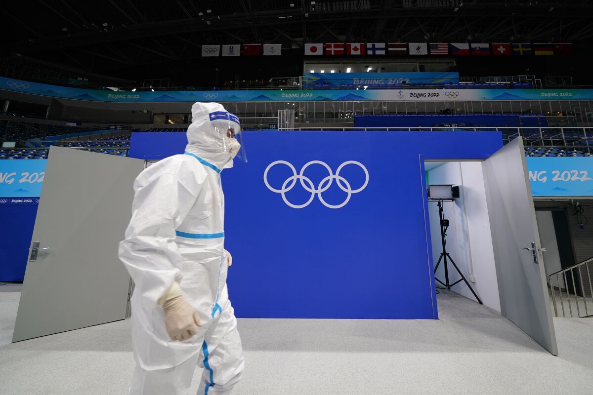 FILE - A worker in protective gear walks past the Olympic rings at the National Indoor Stadium at the 2022 Winter Olympics, Feb. 1, 2022, in Beijing. (AP Photo/Matt Slocum, File)