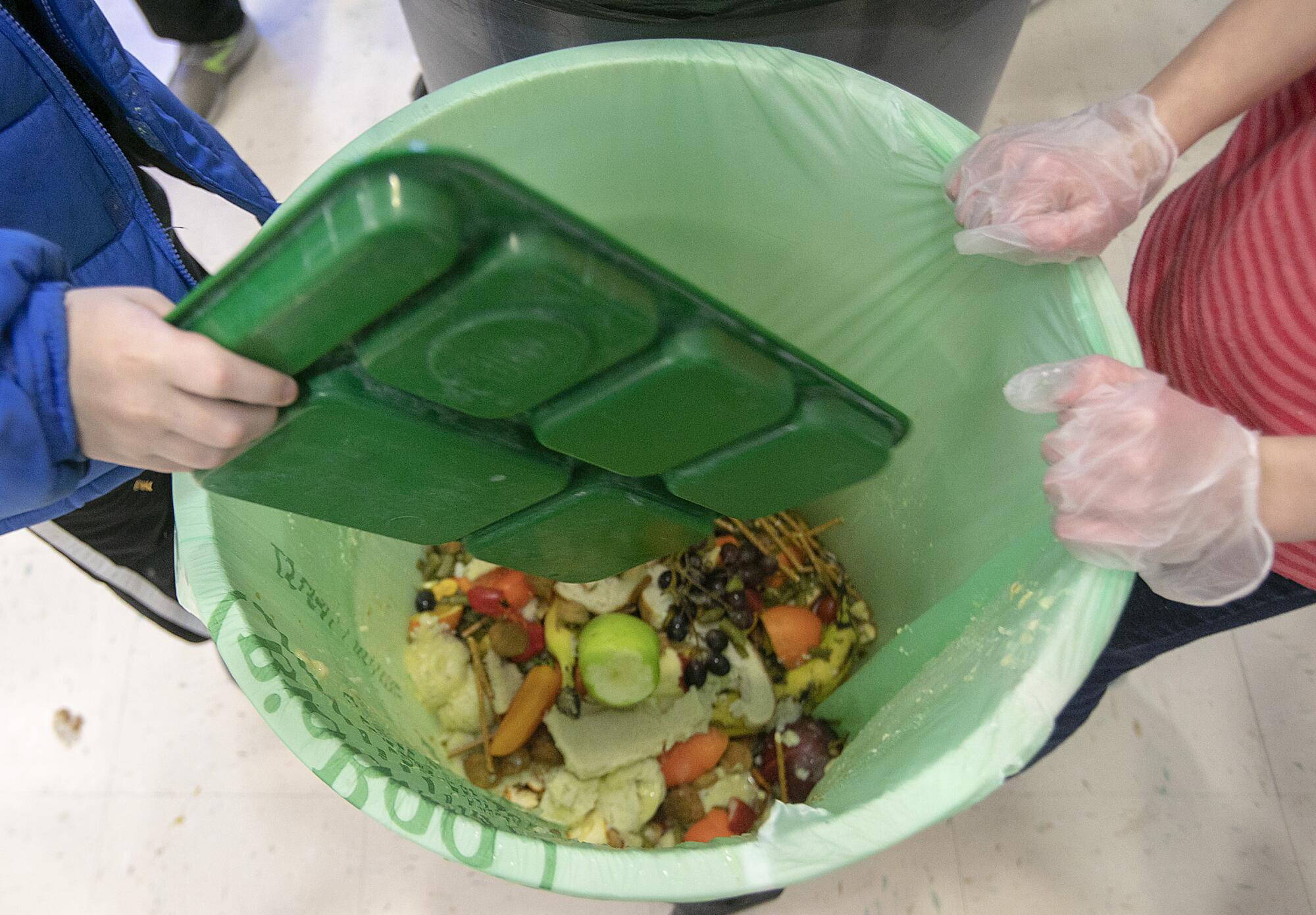 A food tray is emptied into a bin.