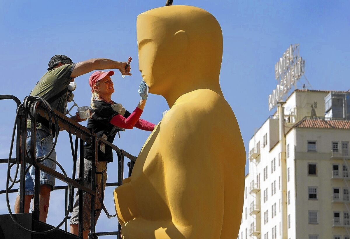 Lead scenic artist Dena D'Angelo, right, and scenic artist Rick Roberts use sand paper to prepare the giant Oscar statue for gold paint before he makes an appearance on the red carpet.
