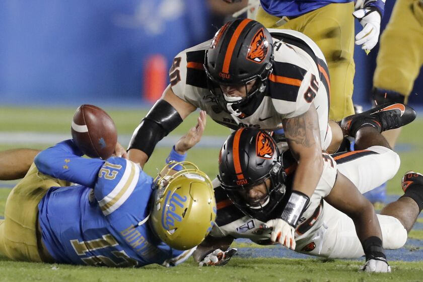 PASADENA,, CALIF. - OCT. 5, 2019. UCLA quarterback Austin Burton loses control of the ball after being tackled by a pair of Oregon State defenders in the third quarter at the Rose Bowl in Pasadena on Saturday night, Oct. 5, 2019. Burton was ruled down on the play before losing the ball. (Luis Sinco/Los Angeles Times)