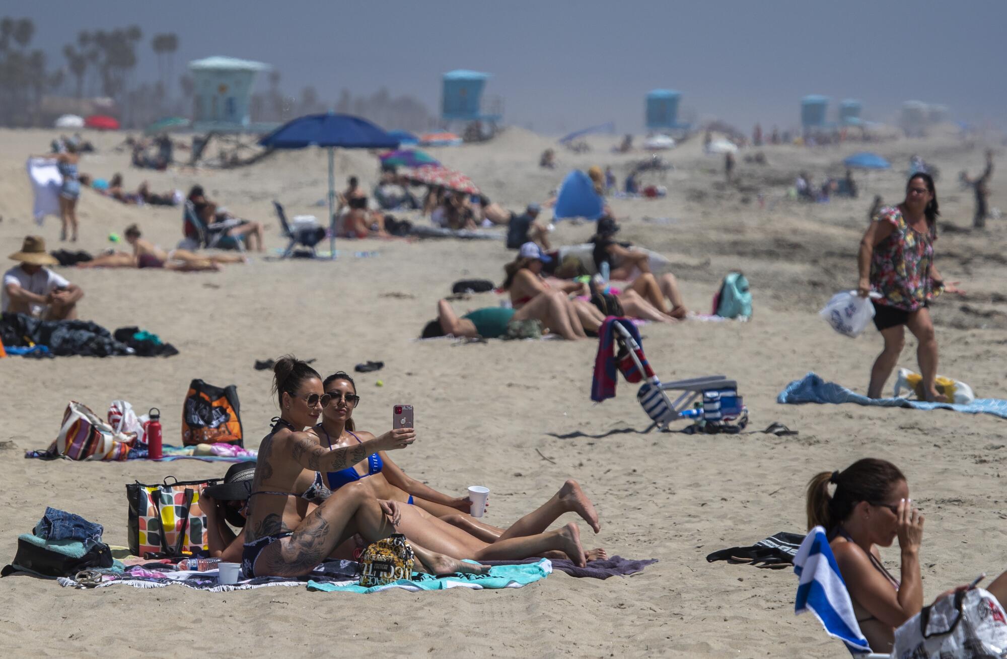 Cailin Healy and an unidentified friend, both of Calabasas, take a selfie together as beachgoers enjoy warm summer-like weather in Huntington Beach amid state and city social distancing regulations mandated by Gov. Newsom.