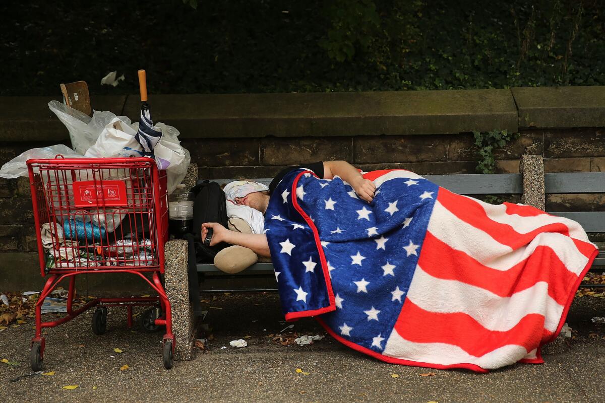 A homeless man sleeps under an American Flag blanket on a park bench on Sept. 10, 2013, in New York City.
