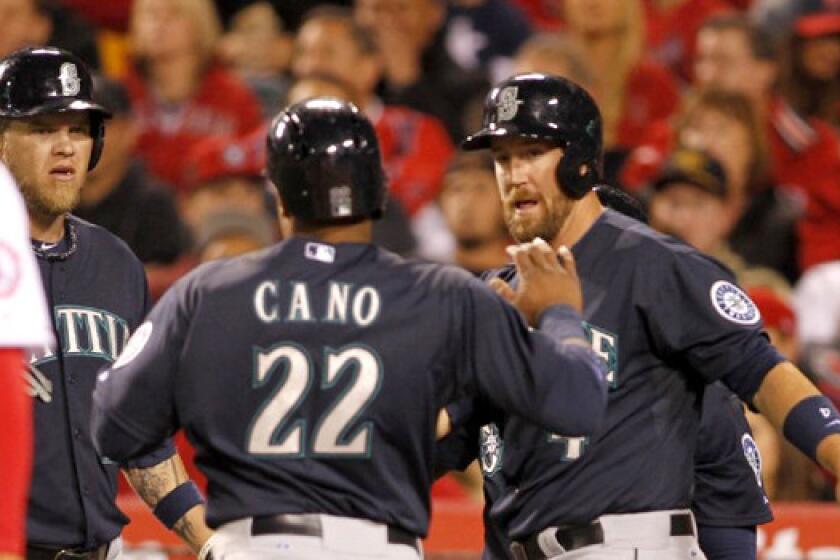 Seattle's Corey Hart, left, and John Buck, right, congratulate Robinson Cano as he scores on a double by Justin Smoak during the third inning of the Angels' 8-3 loss Tuesday to the Mariners.