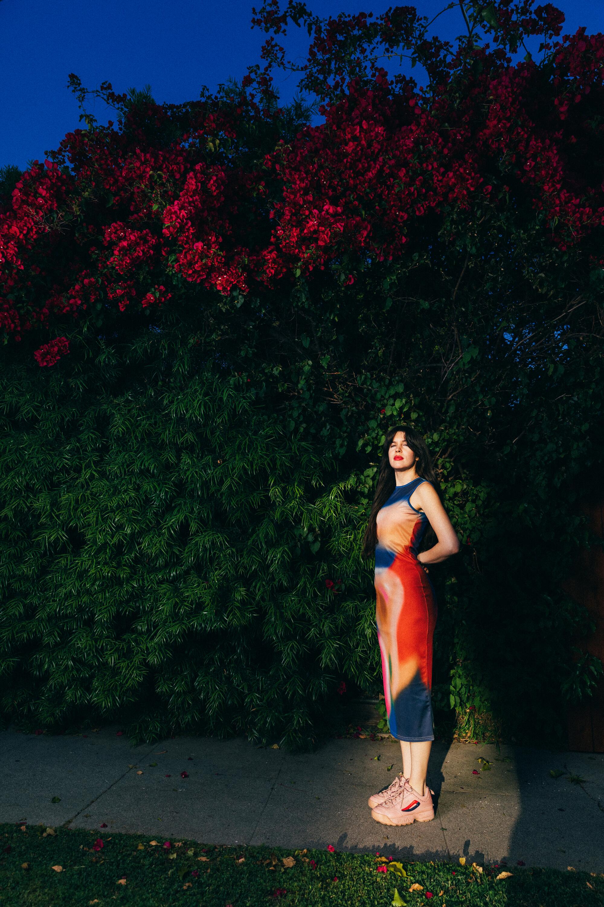 Han Santana-Sayles stands on the sidewalk by tall shrubs in her Pasadena neighborhood. 