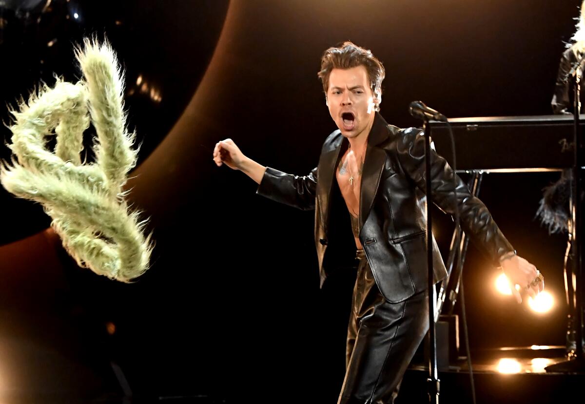  A singer in a black leather jacket and pants tosses a green boa onstage.