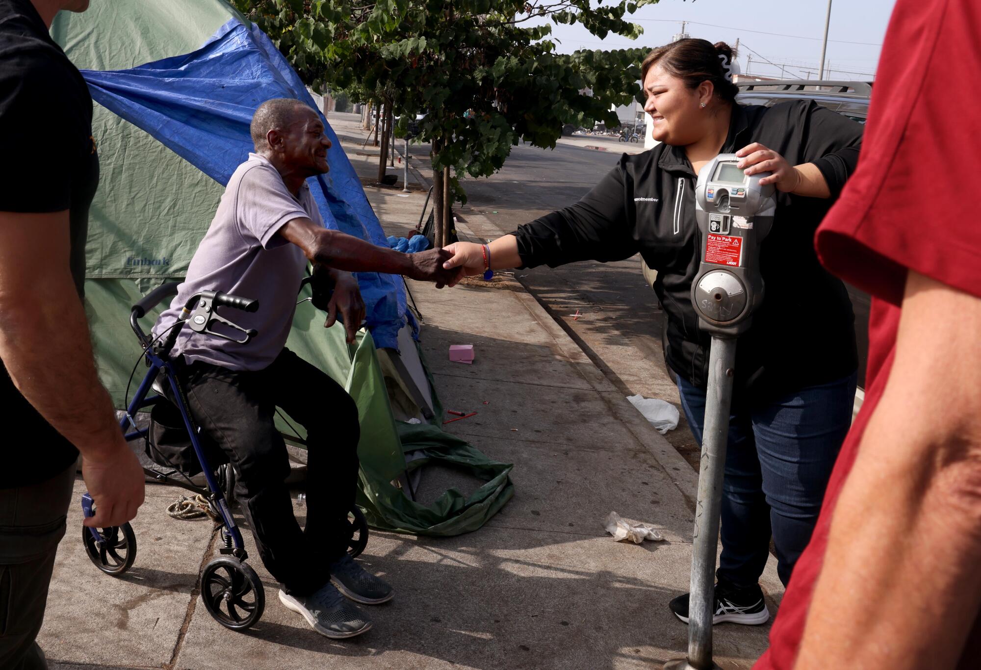 A woman reaches out to a man seated on a walker. 