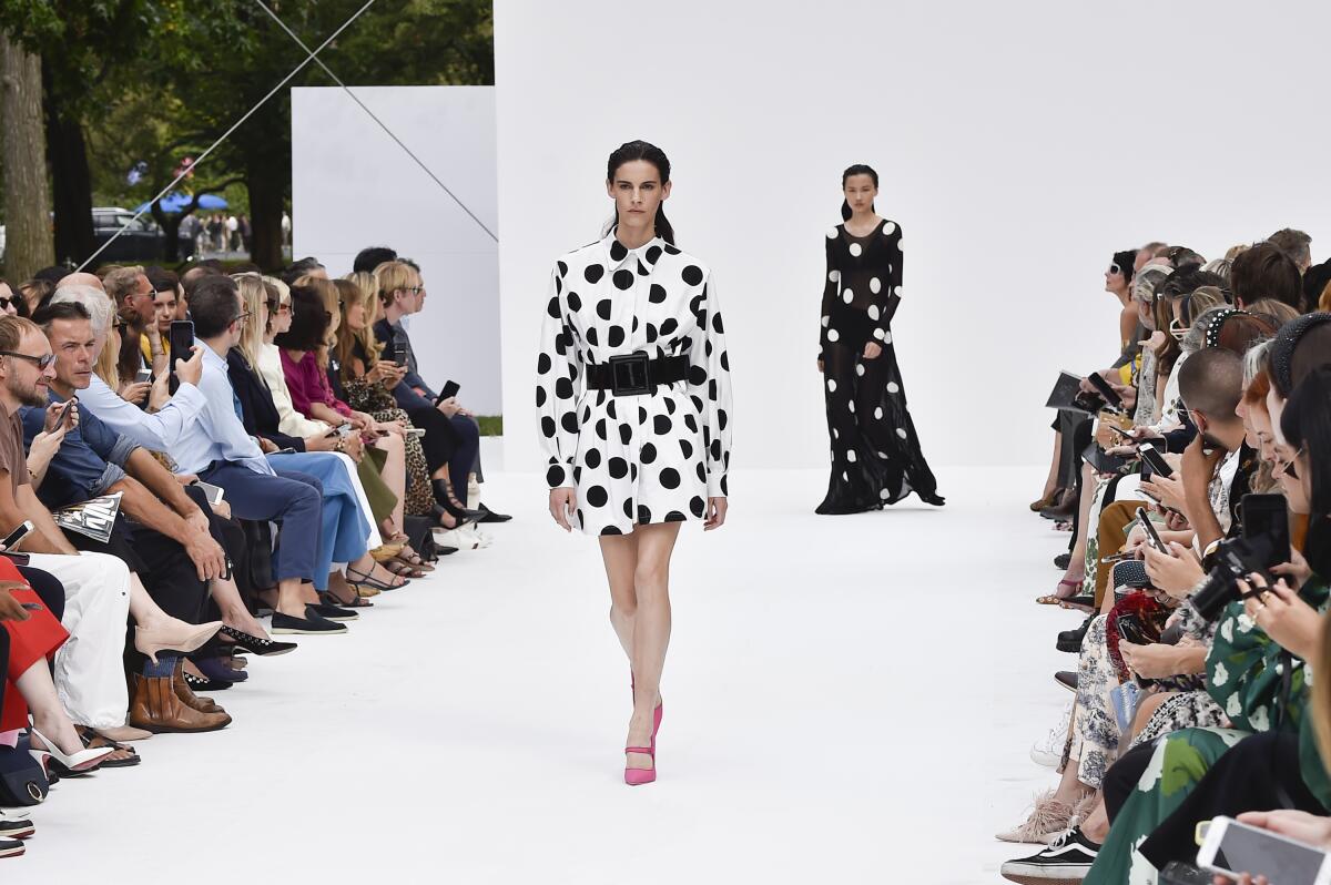 Two models walk the runway in polka-dotted looks from Carolina Herrera: one in a short white dress with black spots; the other, a long black dress with white spots
