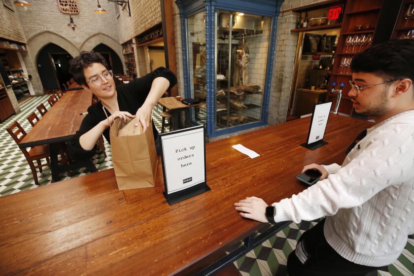 LOS ANGELES, CA - MARCH 18, 2020 Grace Curran, left, restaurant manager packs the take out order for Deni Ershtukaev at Republique (French Restaurant) located at 624 South La Brea as the restaurant continues to serve patrons who love the fine pastries in the morning with a full menu available for carry-out and delivery on Wednesday morning as the restaurant has changed its work flow to accommodate for the coronavirus limitations. (Al Seib / Los Angeles Times)