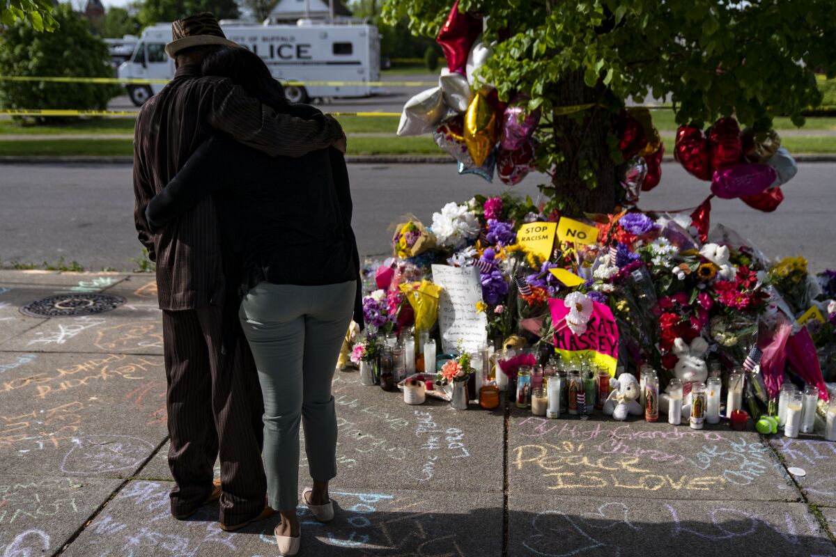 Two people embrace side by side while looking at a memorial