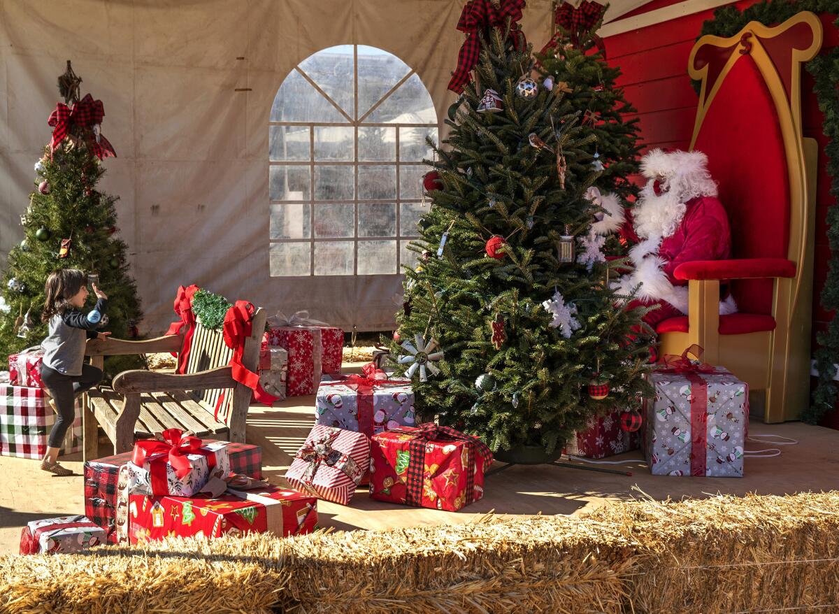 A young girl waves to a Santa seated on a bench