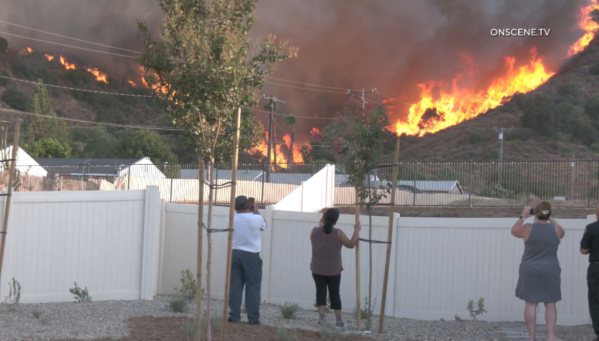 A still from video shows residents filming flames on a hillside from behind a white fence