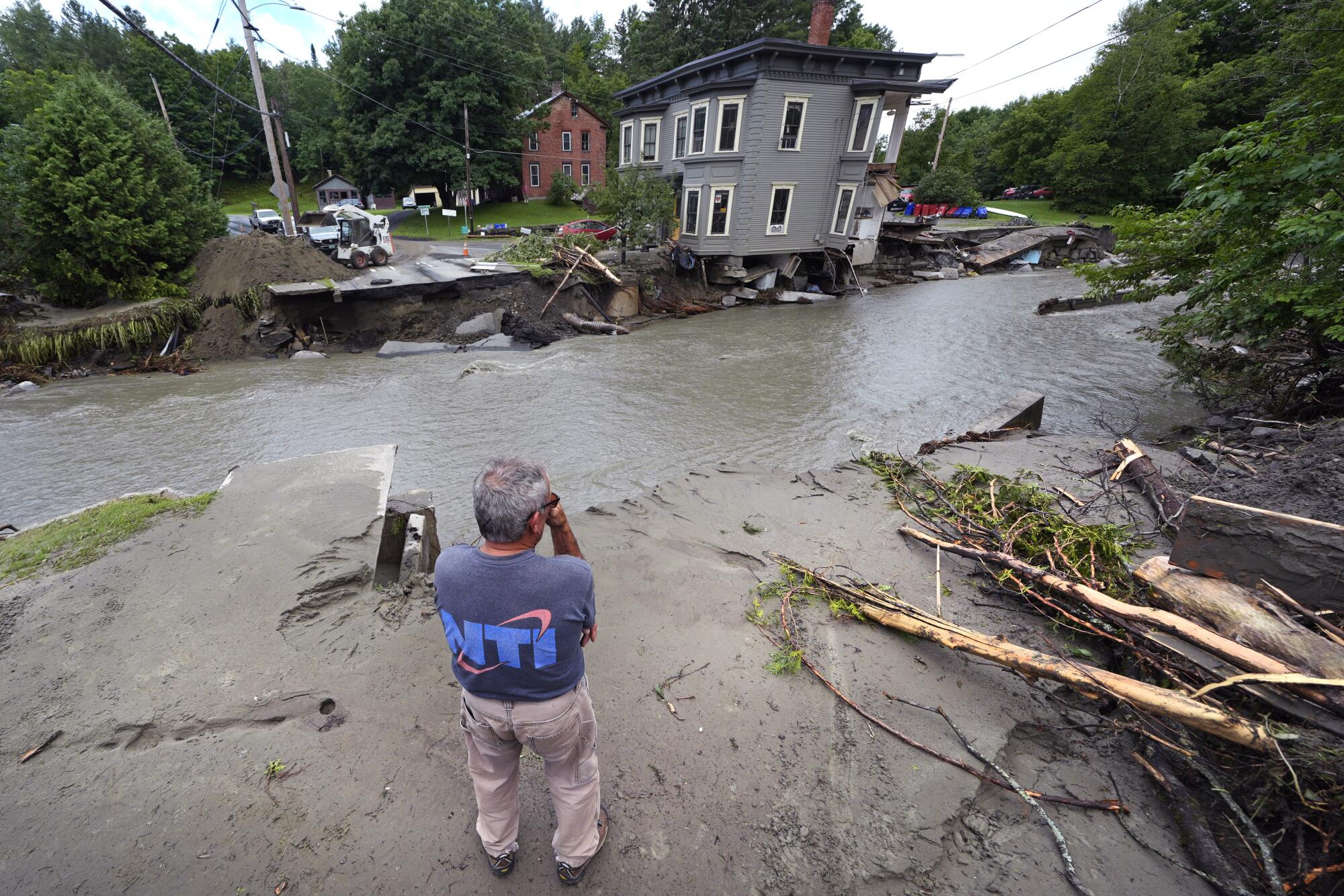 A man surveys a damaged apartment building and a washed-out street.