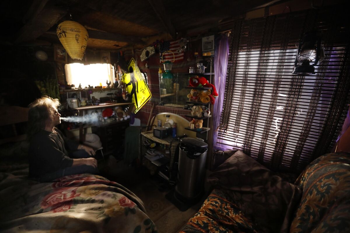 Steve Novak, 52, smokes in the small cabin he constructed in Lancaster. He is a professional drummer and used to play with the group Fatal Thrust. Novak, who recently had a string of heart attacks, refers to his homeless community as "Camp Coolness."
