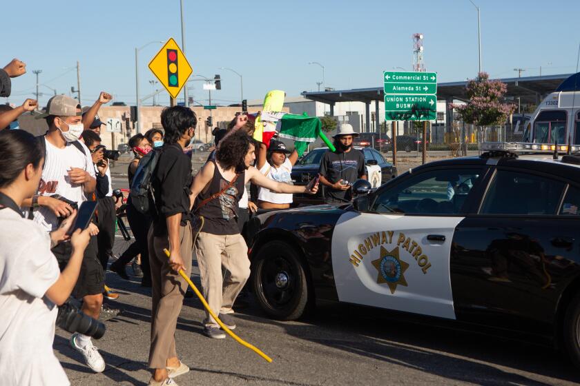 LOS ANGELES, CA - MAY 27: Protesters surround a police vehicle on the 101 freeway near downtown Los Angeles on Wednesday, May 27, 2020 in Los Angeles, CA. A protester smashed the back window with a skateboard. (Gabriella Angotti-Jones / Los Angeles Times)
