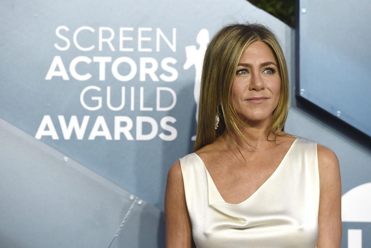 Jennifer Aniston wears a pearl white satin gown and dangly earrings that sparkle. 
