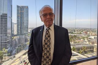 John Baackes, CEO of L.A. Care, stands in front of a window overlooking downtown Los Angeles