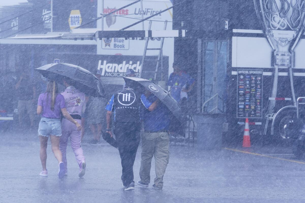 People walk through the track garage area during a rain shower before a NASCAR Xfinity Series auto race Saturday, June 25, 2022, in Lebanon, Tenn. (AP Photo/Mark Humphrey)