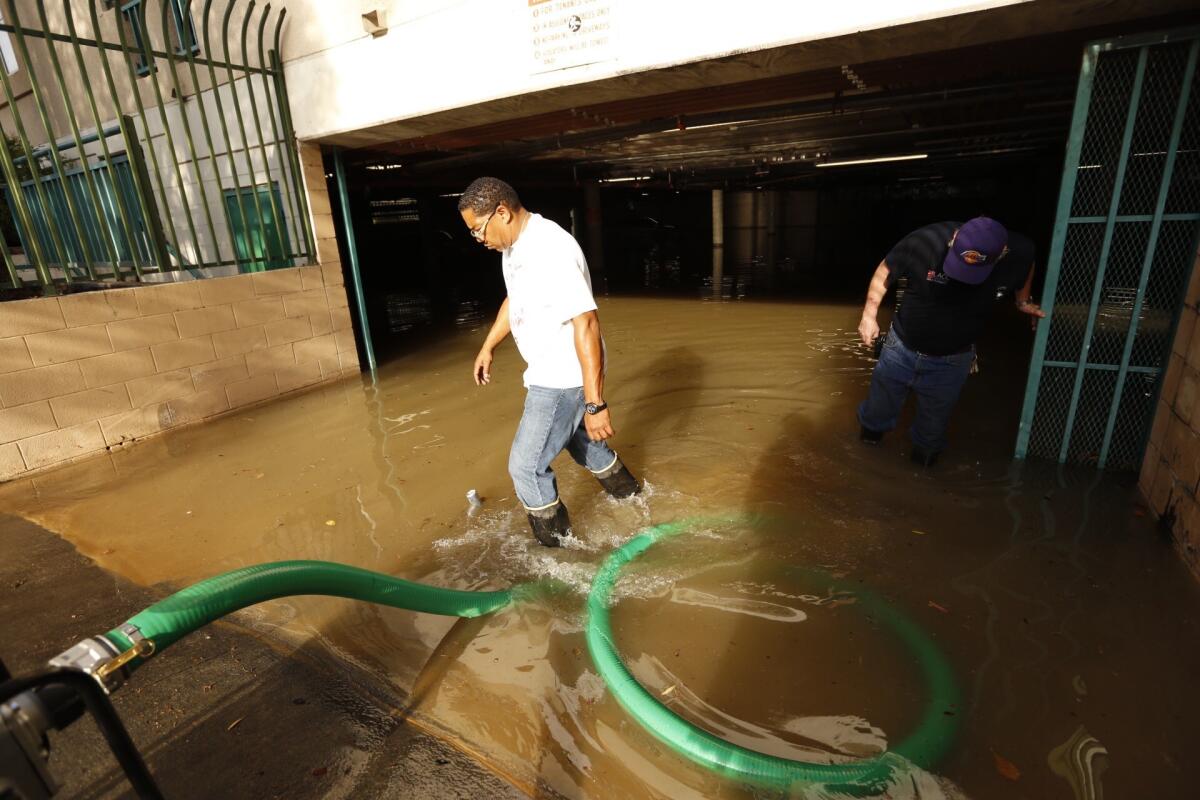 Kelly Cowherd, left and Larry Smith, right, plumbers from nearby L.A. City College, use pumps to drain water from underground parking garage of apartment building on New Hampshire Avenue in East Hollywood after a water main break.