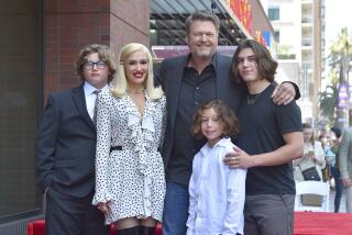 Gwen Stefani in a white dress and Blake Shelton in formal wear pose with three young men at the Hollywood Walk of Fame