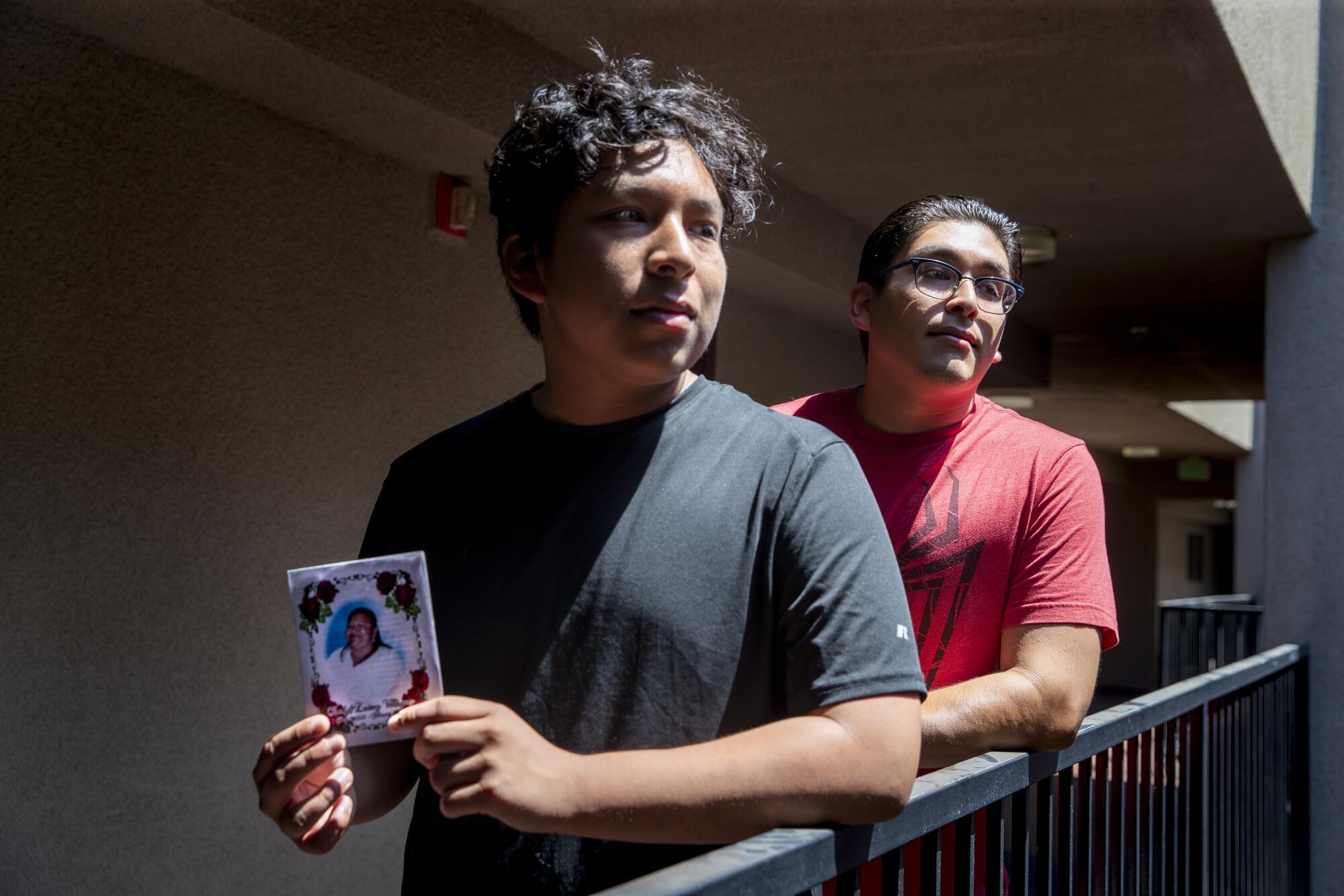 Two brothers pose for a portrait on an outdoor balcony, holding a photo of their late grandmother