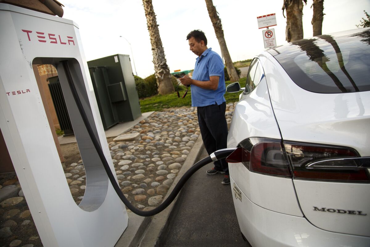 A man stands next to a Tesla charging station, his car plugged in.