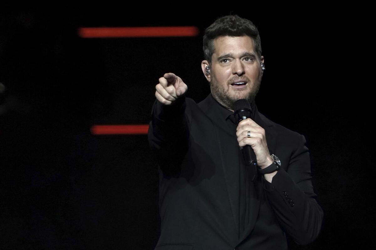 Michael Bublé wearing a black suit points from onstage with one hand while holding a microphone in his other hand