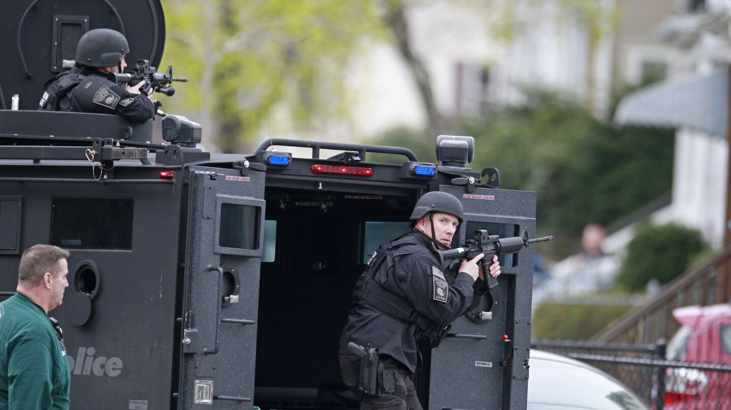 Police take cover as they surround a home while searching for a suspect in the Boston Marathon bombings in Watertown, Mass.