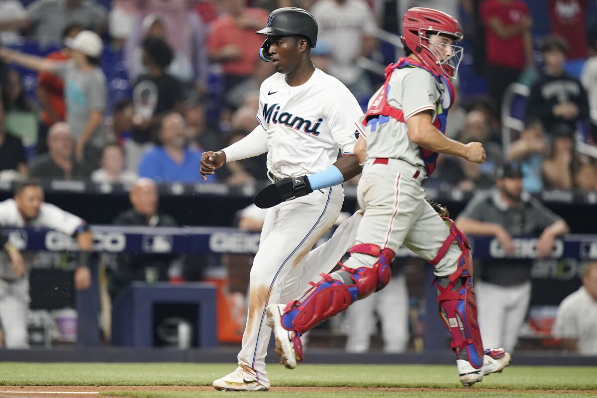 Miami Marlins' Jesus Sanchez, left, scores past Philadelphia Phillies catcher Garrett Stubbs, right, on a sacrifice fly hit by Jesus Aguilar during the fifth inning of a baseball game Friday, April 15, 2022, in Miami. (AP Photo/Lynne Sladky)