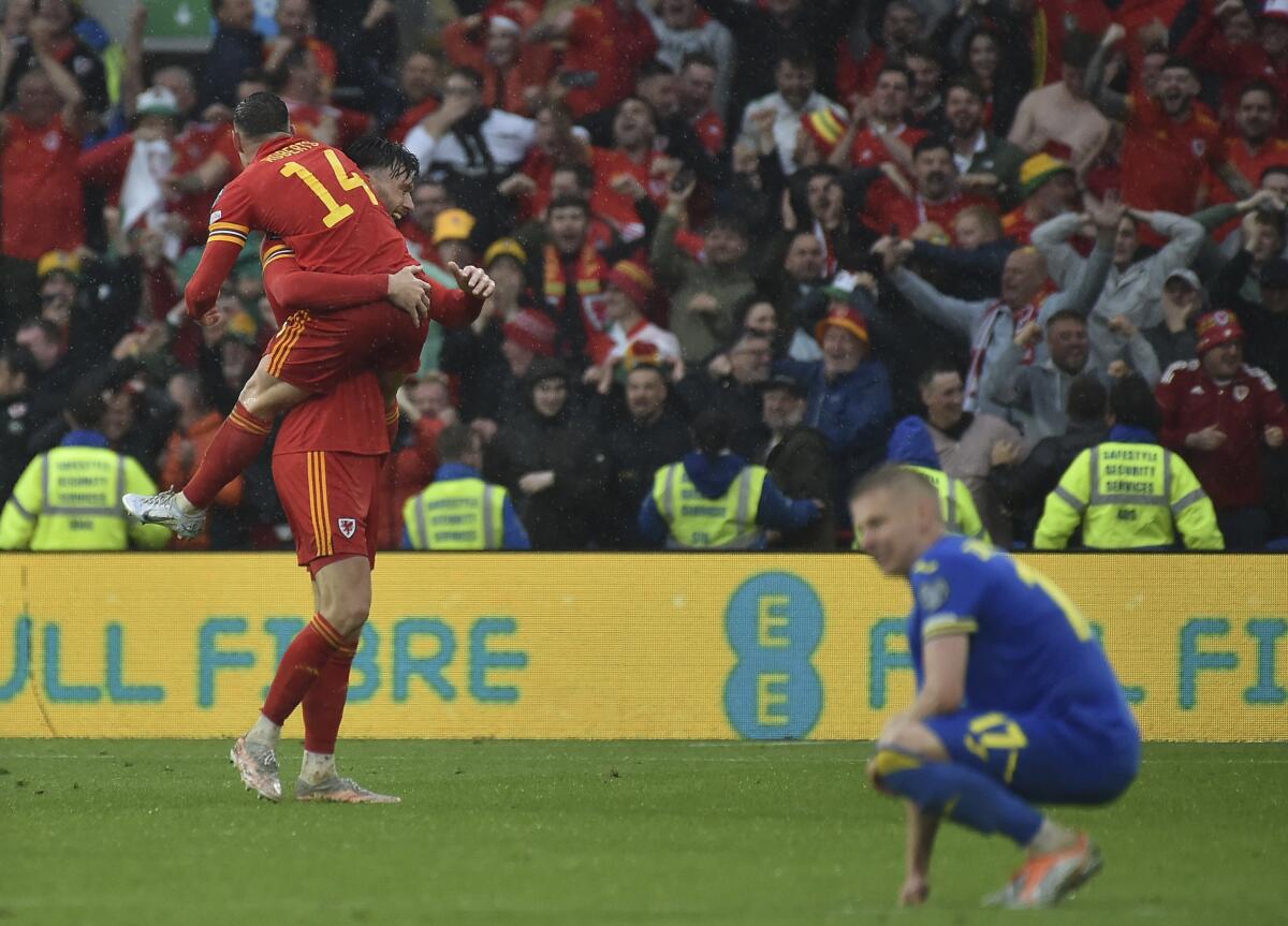 A Welsh soccer player leaps into another's arms while a Ukrainian player kneels on the field after a match.