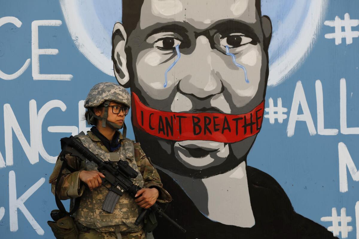 A member of the California National Guard stands in front of a mural depicting George Floyd in Los Angeles. 