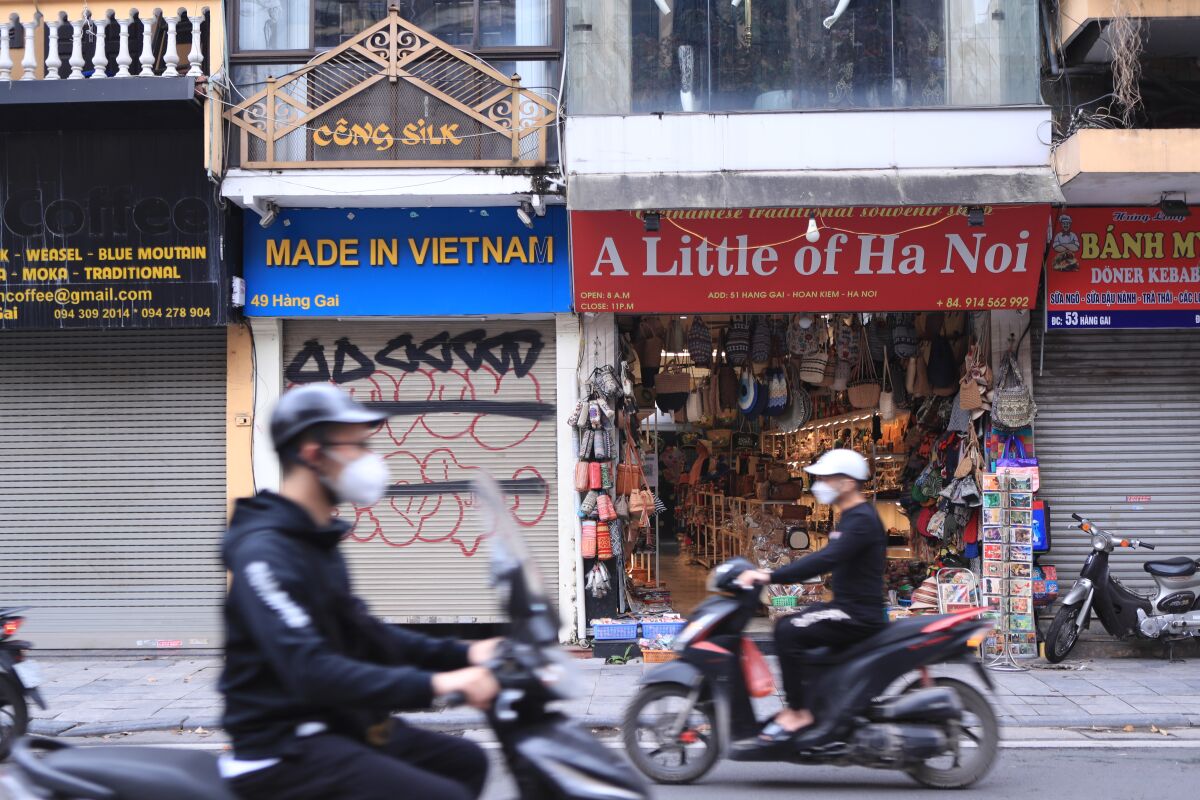 People wearing face masks pass by shops opened and closed in the old quarter of Hanoi, Vietnam on Wednesday, March 16, 2022. Vietnam on Wednesday scrapped quarantine and other travel restrictions for foreign visitors in an effort to fully reopen its border after two years of pandemic-related closure, the government said. (AP Photo/Hau Dinh)