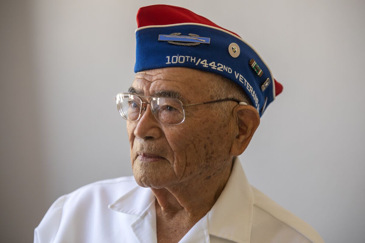 Don Miyada wears a hat with pins and words including "100th / 44nd veterans." 