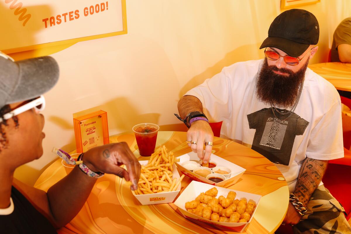 Two people eating tots and dipping sauce together at a table