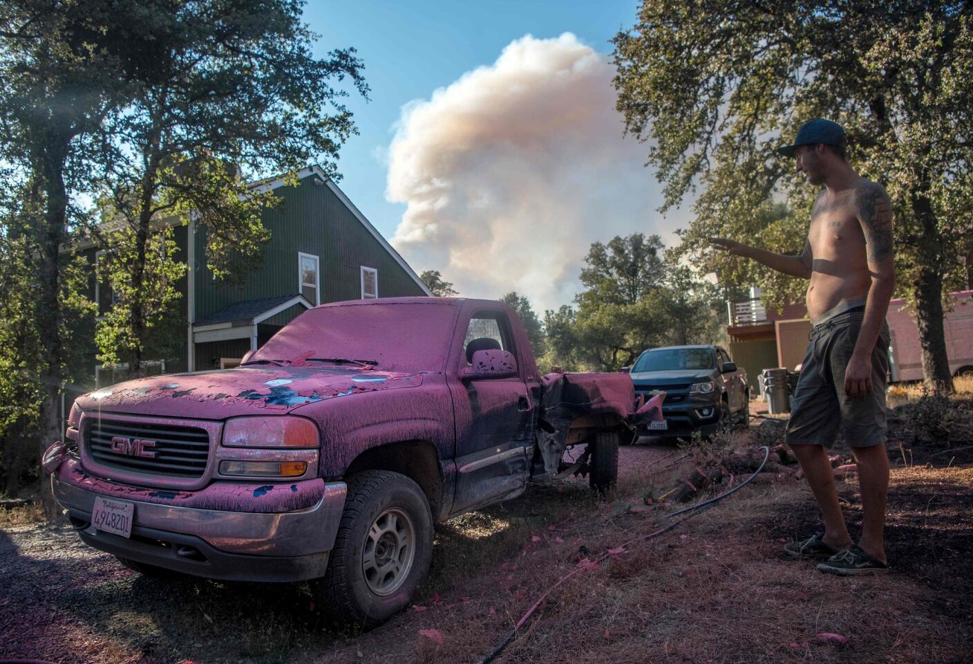 Sean Greenlaw views his truck covered in fire retardant as a smoke plume billows in the background near Oroville.