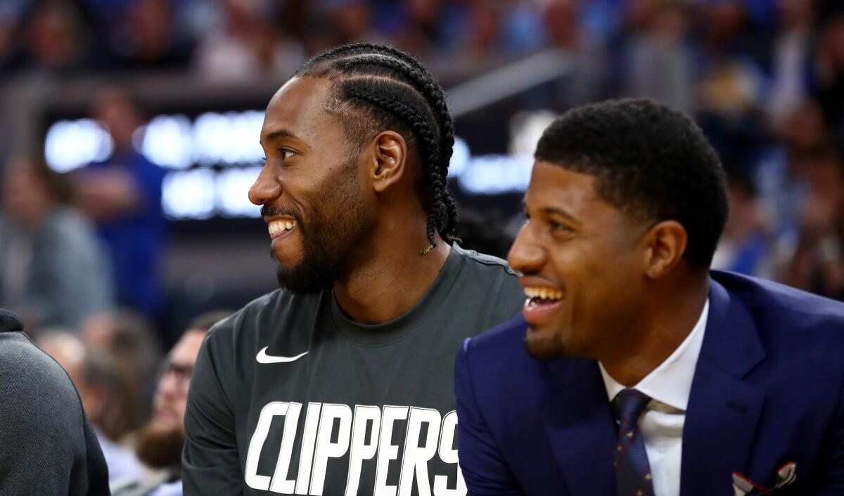 Clippers' Kawhi Leonard, left, and Paul George smile while sitting on the bench during their game against the Golden State Warriors on Oct. 24 in San Francisco.