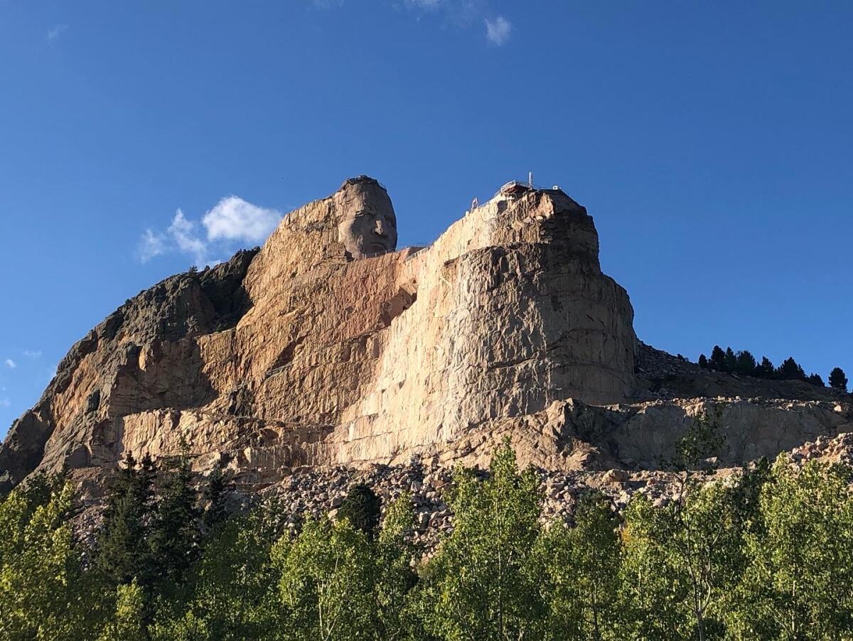 A carving of a man's face atop a mountainous formation, with trees in the foreground