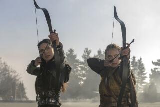 Archers Jessica Green, left, and Maeve Courtier notch arrows and draw their bows in "The Outpost" on The CW.