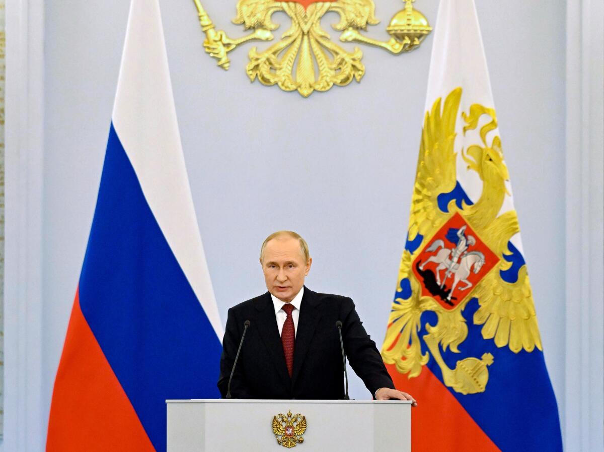 Vladimir Putin standing at a lectern in front of Russia's state and presidential flags.