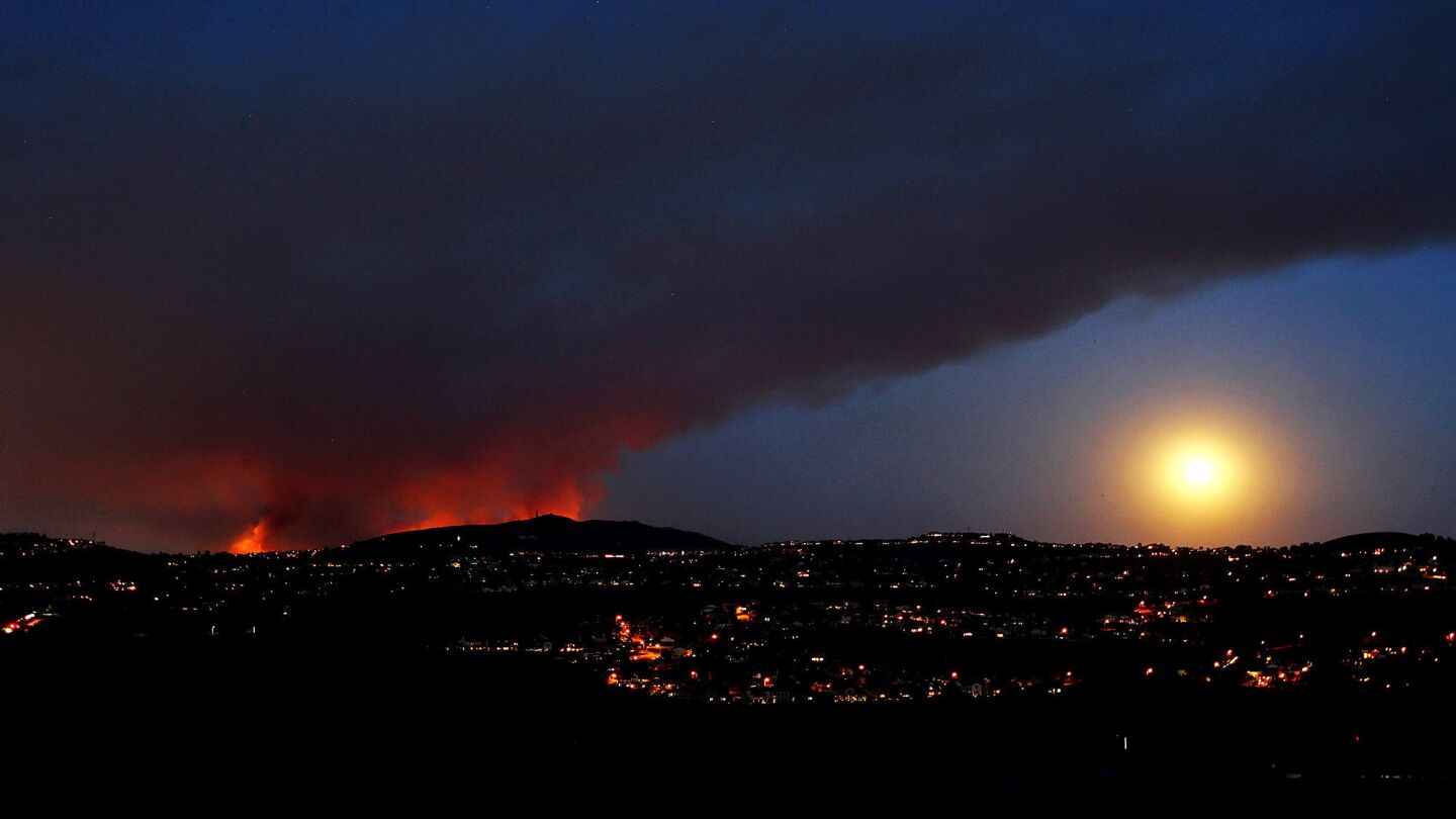 A wildfire burns in San Marcos as the moon rises in a smoky sky as seen from Carlsbad.