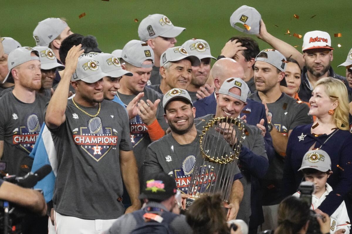 Astros second baseman Jose Altuve holds the Commissioner's Trophy as teammates celebrate World Series title.