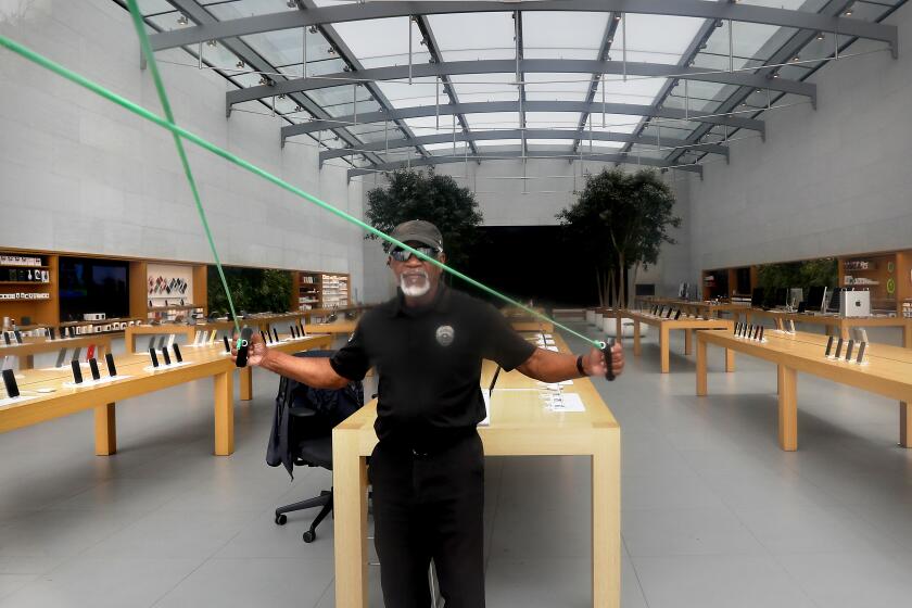 SANTA MONICA, CALIF. - MAY 8, 2020. A security guard gets some exercise while keeping watch on the Apple Store on the Third Street Promenade in Santa Monica on Friday, May 8. 2020. As coronavirus restrictions are loosened, retail shops are allowed to reopen if they provide curbside pickup and practice social distancing. However, most shops on the promenade remained closed on Friday. (Luis Sinco/Los Angeles Times)