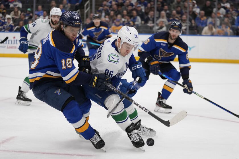 St. Louis Blues' Robert Thomas (18) and Vancouver Canucks' Andrei Kuzmenko (96) battle for a loose puck during the third period of an NHL hockey game Tuesday, March 28, 2023, in St. Louis. (AP Photo/Jeff Roberson)