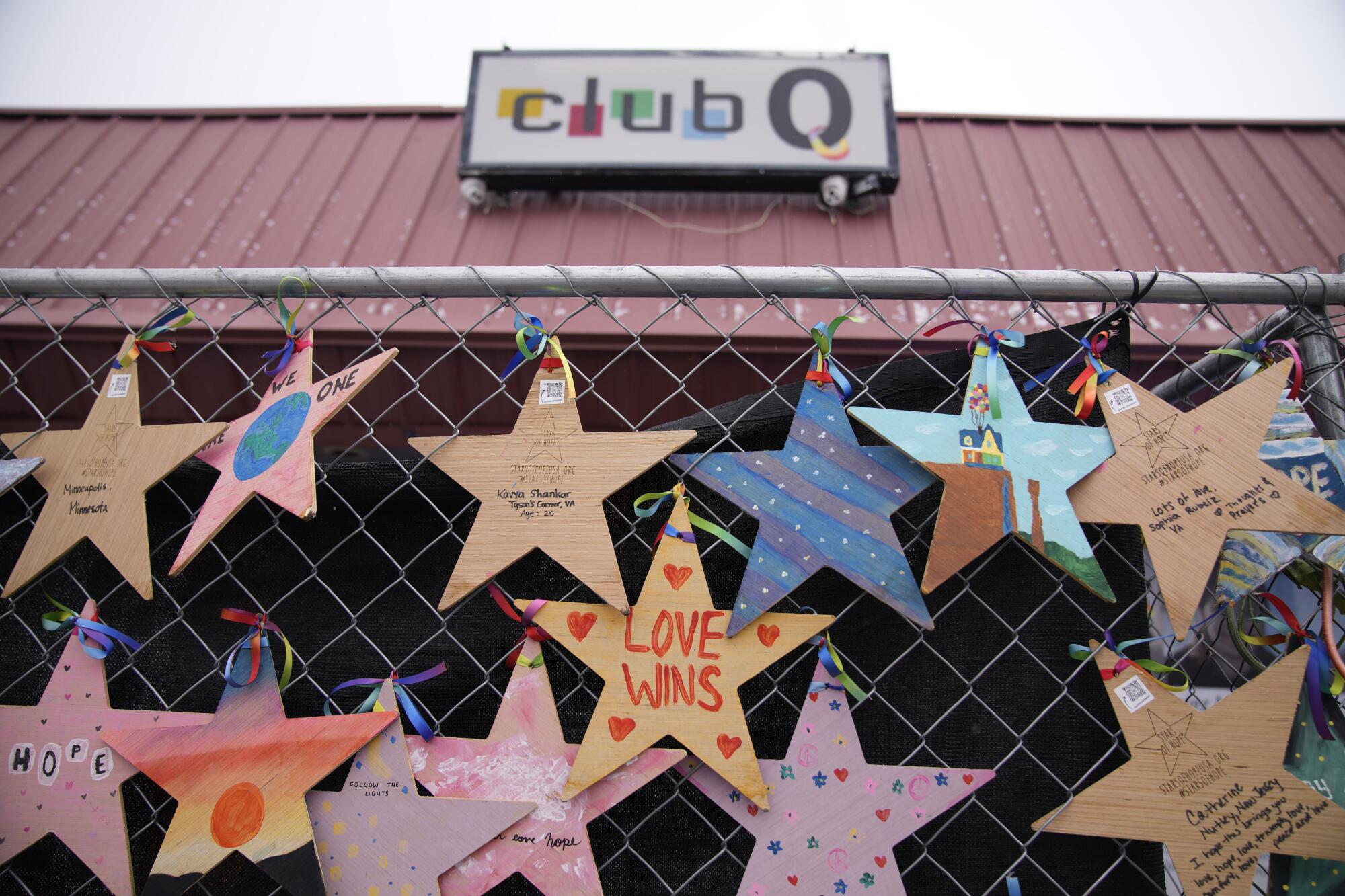 Paper stars hang on a chain-link fence. Behind it, a sign on a building says Club Q