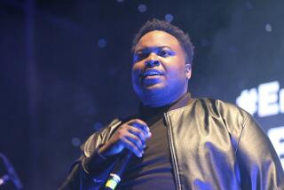 Sean Kingston in a black leather jacket and a black shirt holding a microphone on a stage with blue lights