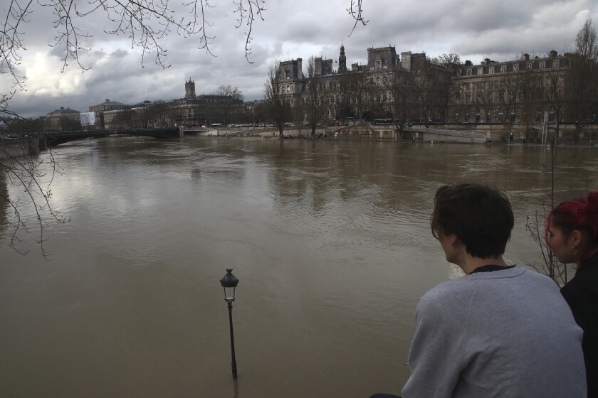 A couple look at the flooded Seine river in Paris, Friday, Feb.5, 2021. The banks of the Seine are flooded after heavy rains cause water levels to rise in the French capital. (AP Photo/Michel Euler)