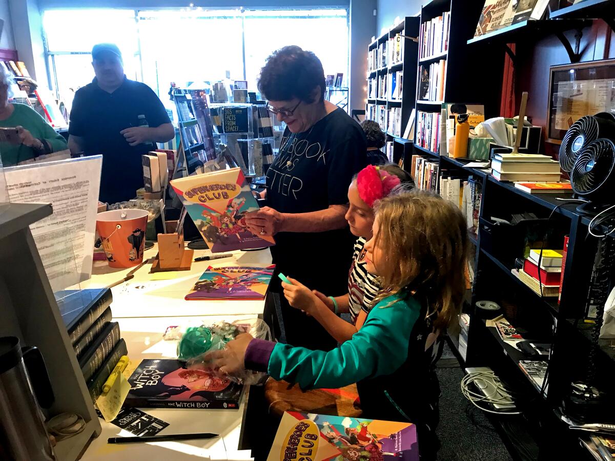A woman in a bookstore helps two children with their books.