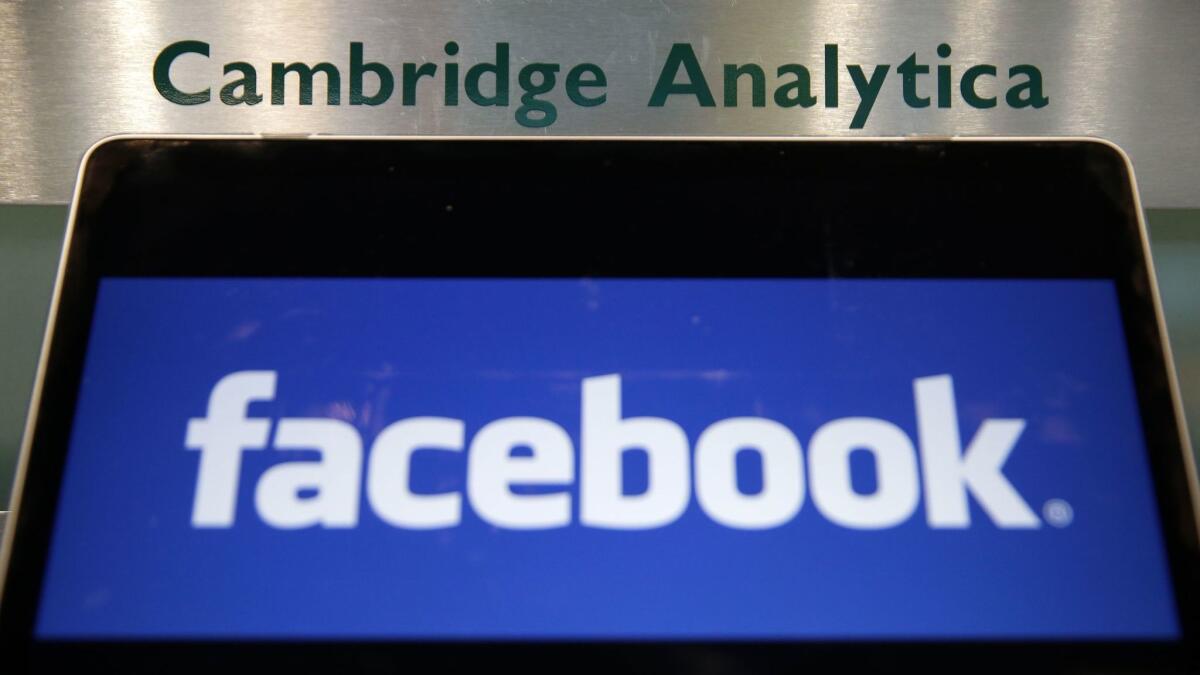 A laptop showing the Facebook logo is held alongside a Cambridge Analytica sign at the entrance to the building housing the offices of Cambridge Analytica in London.