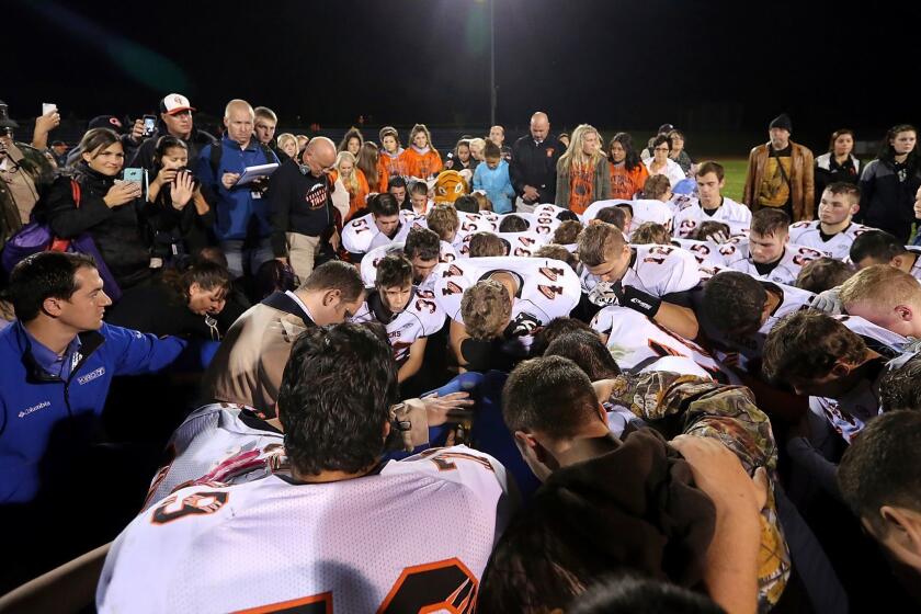 FILE - In this Oct. 16, 2015 file photo, former Bremerton High School assistant football coach Joe Kennedy, obscured at center, is surrounded by Centralia High School football players in Bremerton, Wash., after they took a knee with him and prayed following their game against Bremerton. A federal appeals court ruled Wednesday, Aug. 23, 2017 that the Bremerton School District does not have to immediately re-hire Kennedy, who lost his job after refusing to stop leading players in prayer on the football field after games. (Meegan M. Reid/Kitsap Sun via AP)