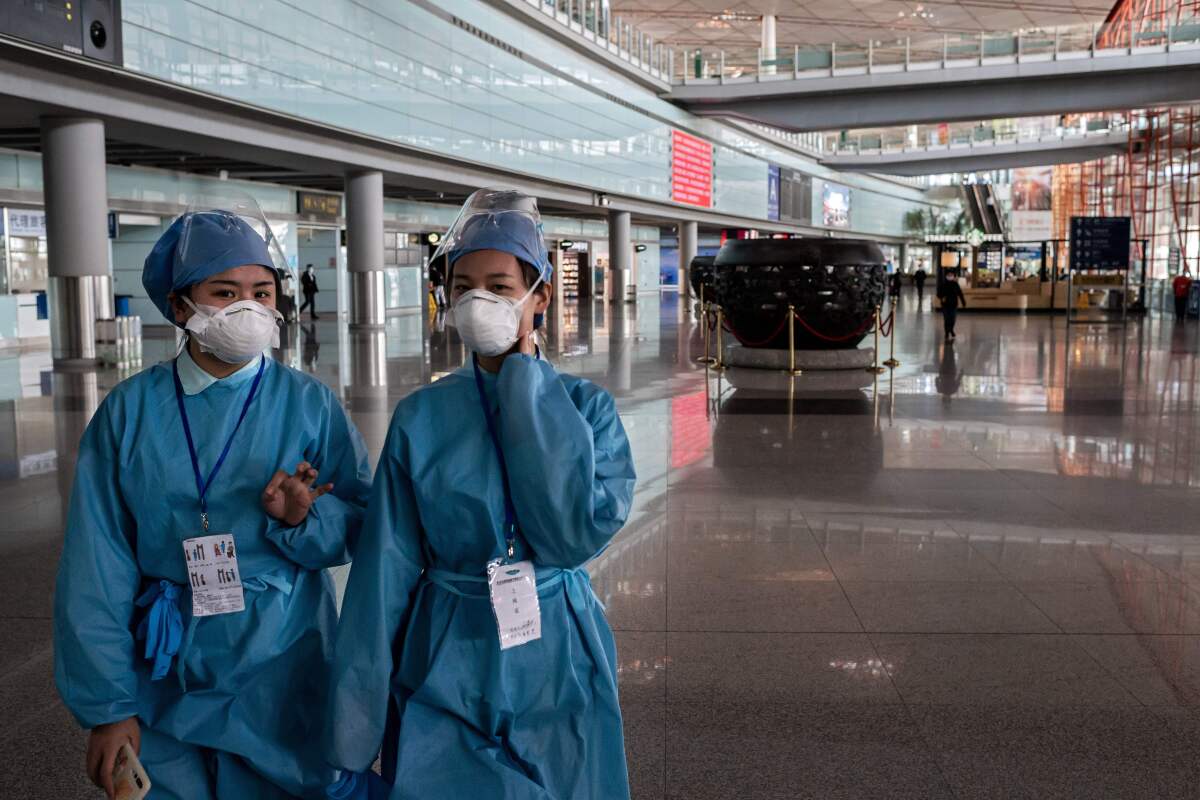 Security workers in protective gear walk through a nearly empty Beijing Capital airport.